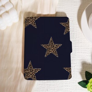 May include: A navy blue tablet case featuring a pattern of leopard print stars. The stars are in varying sizes and are set against a dark blue background. The case has a built-in pocket on the side.