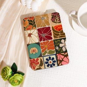 May include: A tablet case with a floral tile pattern in shades of orange, red, and pink. The case has a soft, matte finish and a decorative, artistic style. The design is reminiscent of vintage tile patterns. The case is a rectangle.
