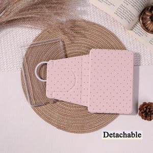 Può includere: Viene mostrata una custodia per telefono rosa con un motivo a pois e una custodia per telefono trasparente. La custodia rosa ha un supporto e un anello bianco. La parola "Detachable" è stampata in basso nell'immagine.