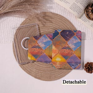 May include: A detachable case with a vibrant geometric pattern depicting sunset and night sky imagery. The case is open, showing a clear protective cover and a white ring. The word "Detachable" is printed at the bottom.