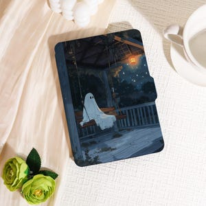 May include: A tablet case with a charming illustration of a ghost on a porch swing under a starry night. The case has a dark blue and grey colour scheme, with a wooden swing and a lantern. The overall theme is spooky and cute, perfect for Halloween.