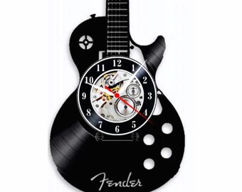 Könnte beinhalten: Schwarze Schallplattenuhr in Form einer Fender E-Gitarre mit einem Zifferblatt in der Mitte. Das Zifferblatt hat ein silber- und goldfarbenes Uhrwerk mit schwarzen Zahlen und Zeigern. Das Zifferblatt ist von einem schwarzen Gitarrenkörper mit einem Fender-Logo umgeben.