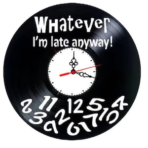 Puede incluir: Reloj de vinilo negro con texto blanco que dice "Whatever I'm late anyway!". La esfera del reloj es blanca con manecillas negras y un segundero rojo. Números blancos alrededor de la esfera.