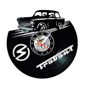 Pode incluir: Relógio de vinil preto com uma silhueta de um carro vintage e a palavra "TRIUMPH" em letras brancas. O mostrador do relógio é visível com algarismos romanos.