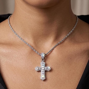 Peut inclure: Collier argenté avec un pendentif en forme de croix orné de pierres précieuses claires et étincelantes. La chaîne est torsadée. Le collier est présenté sur un fond de teint.