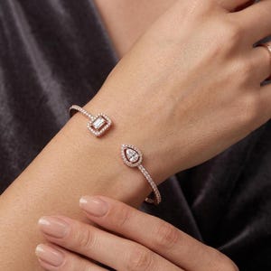 Peut inclure: Bracelet manchette ouvert en or rose orné d'un oxyde de zirconium carré et d'un oxyde de zirconium en forme de poire. Le bracelet est incrusté de petits oxydes de zirconium transparents. Le bijou est présenté sur un poignet.