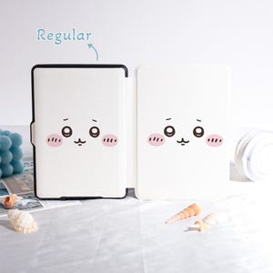 Pu&ograve; includere: Custodia bianca per tablet con un design a forma di viso di cartone animato. La custodia &egrave; aperta, rivelando l'interno e il design sul davanti. Il design presenta due grandi occhi, guance rosee e una bocca piccola. La parola "Regular" &egrave; scritta sopra la custodia.