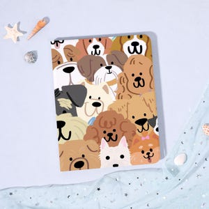May include: A rectangular notebook featuring a colorful illustration of various dog breeds. The dogs are depicted with cartoon-like features in shades of brown, tan, and white, creating a playful and cheerful design. The notebook is set against a light blue background.