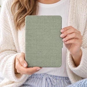 Könnte beinhalten: Eine e-Reader-Hülle in Salbeigrün mit strukturierter Stoffoberfläche. Das rechteckige Etui hat ein schmales Profil und ein umlaufendes Design, das die Vorderseite des Geräts abdeckt und für ein einheitliches Erscheinungsbild sorgt.