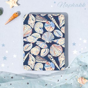 Pode incluir: Uma capa retangular para leitor de e-books com fundo azul escuro e um padrão repetitivo de várias conchas em tons de creme, azul claro e laranja suave. A palavra Naphakk está impressa no canto superior direito em fonte cursiva.