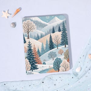 May include: A notebook with a winter landscape design. The cover features a snowy mountain scene with evergreen trees, bare trees, and a light blue sky. The notebook is rectangular and has rounded corners.