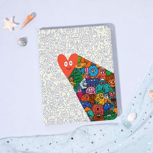 May include: A rectangular notebook with a whimsical design. The cover features a large red heart with a smiling face, and a colorful illustration of cartoon characters. The background is a pattern of small, gray cartoon faces.