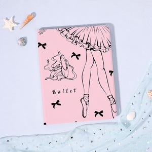 Peut inclure: Cahier rose sur le thème du ballet. La couverture présente un dessin au trait noir des jambes et des pointes d'une ballerine, un tutu et le mot "Ballet". Des nœuds noirs sont dispersés sur la couverture.