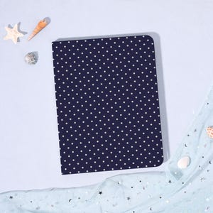 May include: A navy blue notebook with a white polka dot pattern. The notebook is rectangular with rounded corners. Decorative seashells and a starfish are in the background.
