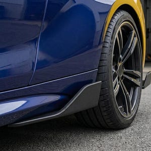 Puede incluir: Primer plano de un coche azul y dorado con un neumático y una llanta negros. El coche tiene una falda lateral negra. El neumático es negro con una llanta negra.