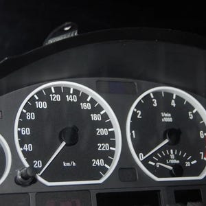 May include: Car dashboard with various gauges, including a speedometer up to 240 km/h. Other dials display fuel level, engine RPM, and temperature. White markings and needles are set against a black background.