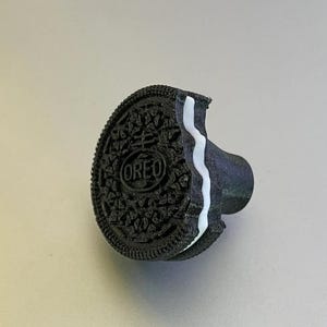 May include: A black and white Oreo cookie-shaped cabinet knob. The knob has a bite taken out of it, revealing the white cream filling. The word "OREO" is visible on the cookie. This unique knob adds a playful touch to any cabinet or drawer.