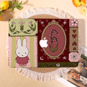 May include: A laptop skin featuring a white rabbit character on a pink and green striped background, alongside a dark red panel with an oval frame containing a lily of the valley illustration, white stars, and a cutout for an Apple logo.