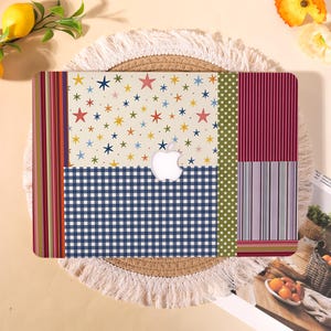 May include: A colorful laptop case with a patchwork design. The case features a cream background with stars, a blue and white checkered pattern, and vertical stripes in various colors. An Apple logo is visible.