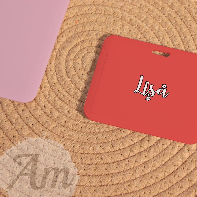 May include: A red rectangular card with the name "Lisa" in a cursive font. The card is on a woven surface, with a pink rectangular object in the upper left corner. The name "Am" is also visible.