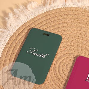 May include: A dark green luggage tag with the name "Smith" in elegant white script. The tag has a rectangular shape with a small hole at the top. The background is a woven, light brown surface.