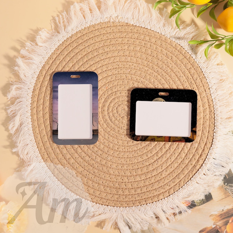 May include: Two rectangular ID badge holders with a white insert. One has a dusk scene, the other a night scene. They are on a round, woven placemat with a fringed edge. The word "Am" is visible in the bottom left corner.