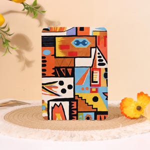 May include: A rectangular case with a vibrant, geometric design in orange, yellow, blue, and brown. The pattern features abstract shapes and lines, creating a colorful, artistic look. The case is likely for a tablet or similar device.