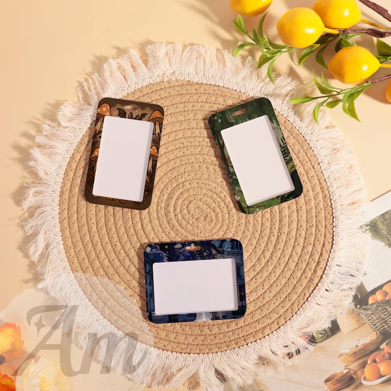 May include: Three rectangular ID badge holders with different decorative borders. One has a brown border with orange mushroom designs, another has a green border with a leaf pattern, and the third has a blue border with a floral design.
