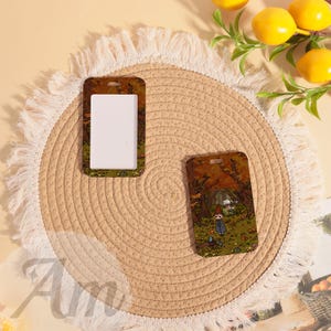 May include: Two rectangular ID badge holders with a forest scene design. One holder has a white insert, the other features the full illustration. The holders are brown with a small hole at the top for a lanyard.