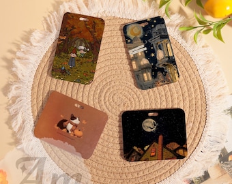 May include: Four rectangular decorative tags with different illustrations. One tag features a forest scene, another a night cityscape, a third a cat with a pumpkin, and the last a spooky night scene with a full moon. Each tag has a hole at the top.