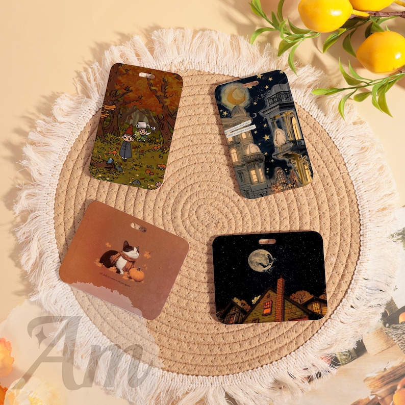 May include: Four rectangular decorative tags with different illustrations. One tag features a forest scene, another a night cityscape, a third a cat with a pumpkin, and the last a spooky night scene with a full moon. Each tag has a hole at the top.