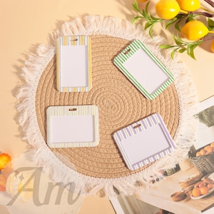 May include: Four rectangular badge holders with striped borders in yellow, green, and purple, each with a clear window. The holders are arranged on a round, woven placemat with a fringed edge. Decorative lemons and text are in the background.
