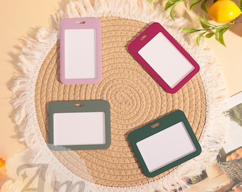 May include: Four colorful ID badge holders in pink, burgundy, and two shades of green, each with a white insert. The holders are arranged on a round, woven placemat with a fringed edge. Lemons and greenery are in the background.