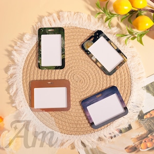 May include: Four rectangular ID badge holders with different designs. One has a green and black camouflage pattern, another features a night sky with a moon and stars, a third is brown, and the last has a purple and blue sunset scene.