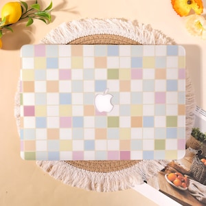 May include: A laptop hard shell case featuring a grid pattern of small squares in pastel shades of pink, blue, yellow, and green. The case has a central cutout revealing the white Apple logo, providing a protective cover for the device exterior.