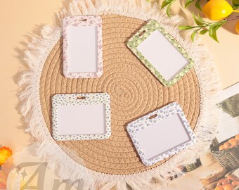 May include: Four floral-patterned ID badge holders in pink, green, blue, and white. The holders are rectangular with a clear window and a small hole at the top. They are arranged on a round, woven mat.