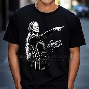 May include: A black short-sleeved t-shirt featuring a white graphic illustration of a basketball player with a ponytail pointing forward. The player wears a jersey with the number 8 and the text Salesforce. A white signature is printed next to the player.