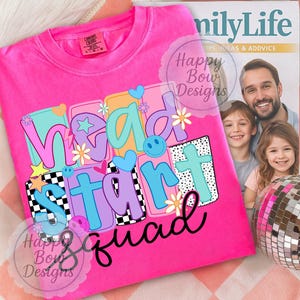 May include: A bright pink crew neck t-shirt with the words "Head Start Squad" in a colorful, playful design. The design includes hearts, stars, flowers, and a checkerboard pattern. The shirt is displayed on a patterned surface.