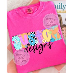 Pu&ograve; includere: Una maglietta rosa acceso con la scritta "CUSTOM" in lettere colorate e giocose. La parola "designs" &egrave; scritta in corsivo nero sotto. Il design include fiori, una faccina sorridente e un motivo a scacchi.