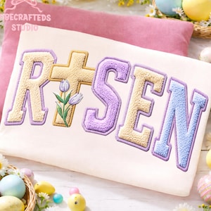 Peut inclure: Un sweat-shirt crème avec le mot "RISEN" dans une police de style universitaire. Les lettres sont dans des tons de jaune, de violet et de bleu, avec une croix et un graphisme de tulipe. L'image a un thème de Pâques.