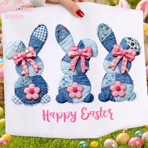 Może przedstawiać: Biała tkanina z trzema aplikacjami z dżinsowych królików, każdy z różową kokardą i kwiatkiem. Króliki są patchworkowe z niebiesko-białymi wzorami. Napis "Happy Easter" jest w kolorze różowym.