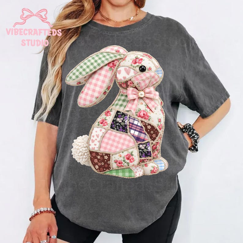 May include: Dark gray t-shirt featuring a patchwork bunny design with pink, green, and floral patterns. The bunny has a pink bow and a fluffy white tail. The text "VIBECRAFTEDS STUDIO" is in the upper left corner.