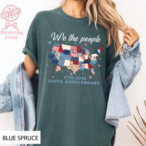 May include: A teal t-shirt featuring the phrase "We the people" above a patchwork map of the USA. The design includes the text "1776-2026 250TH ANNIVERSARY". The shirt is a celebration of the USA's history.