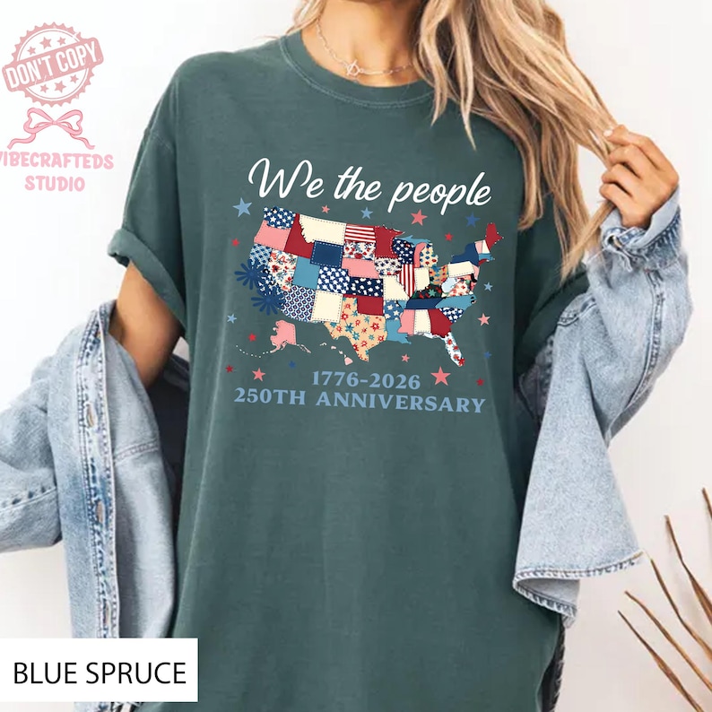 May include: A teal t-shirt featuring the phrase "We the people" above a patchwork map of the USA. The design includes the text "1776-2026 250TH ANNIVERSARY". The shirt is a celebration of the USA's history.