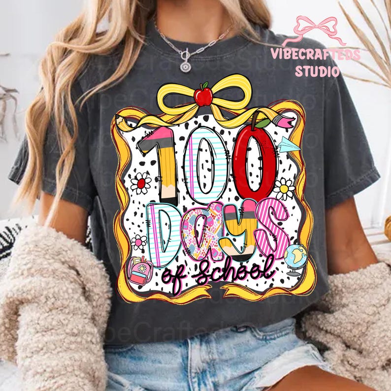 Puede incluir: Camiseta gris oscuro con un gr&aacute;fico colorido que celebra "100 d&iacute;as de escuela". El dise&ntilde;o incluye una manzana roja, l&aacute;pices y las palabras "100 d&iacute;as de escuela" en una fuente l&uacute;dica, ideal para estudiantes y profesores.