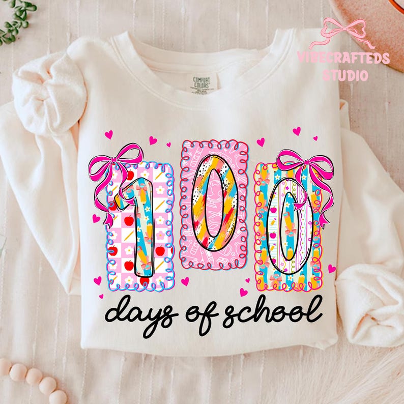 May include: Cream-colored sweatshirt with a colorful "100 days of school" design. The design features the numbers "100" in decorative frames, bows, and hearts. The text "days of school" is written in a black script font.