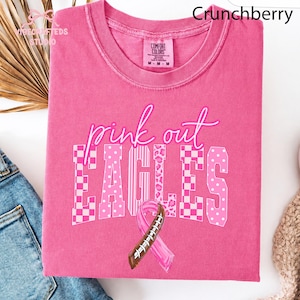 May include: A pink short-sleeve t-shirt with a crew neckline. The graphic features the text "pink out" in white script above the word "EAGLES" in block letters with various pink patterns, and a pink awareness ribbon with football laces.