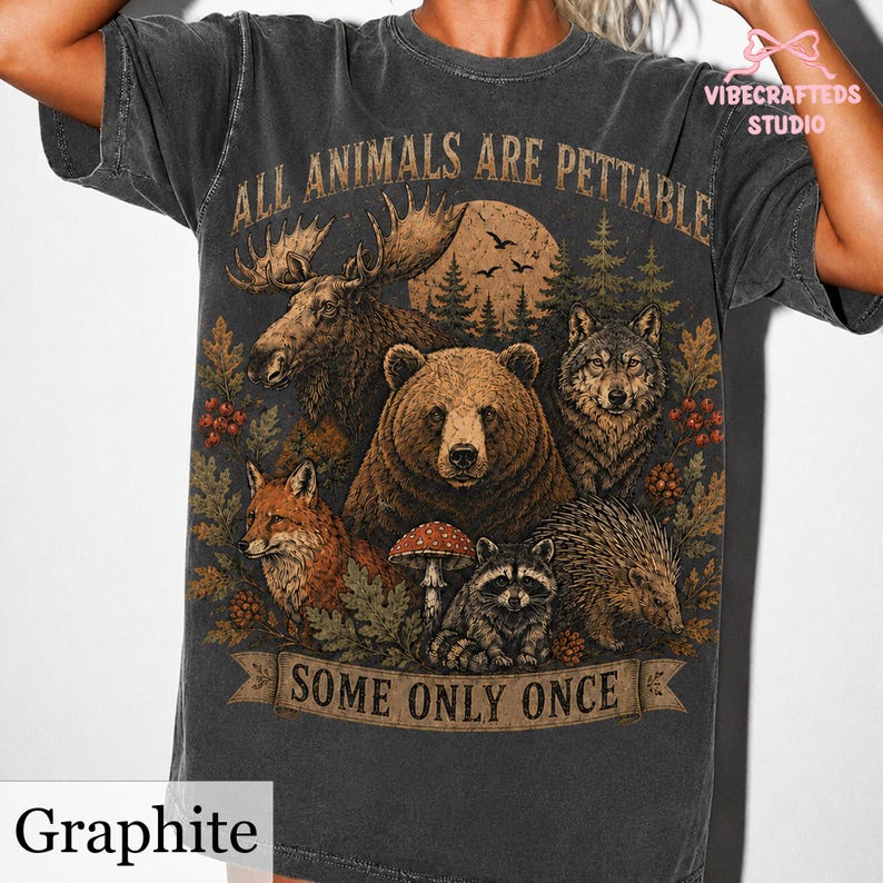 Pu&ograve; includere: Una t-shirt grigio antracite con una stampa grafica raffigurante un alce, un orso, un lupo, una volpe, un procione e un riccio circondati da elementi boschivi. Il testo recita ALL ANIMALS ARE PETTABLE SOME ONLY ONCE. Include luna e pini.