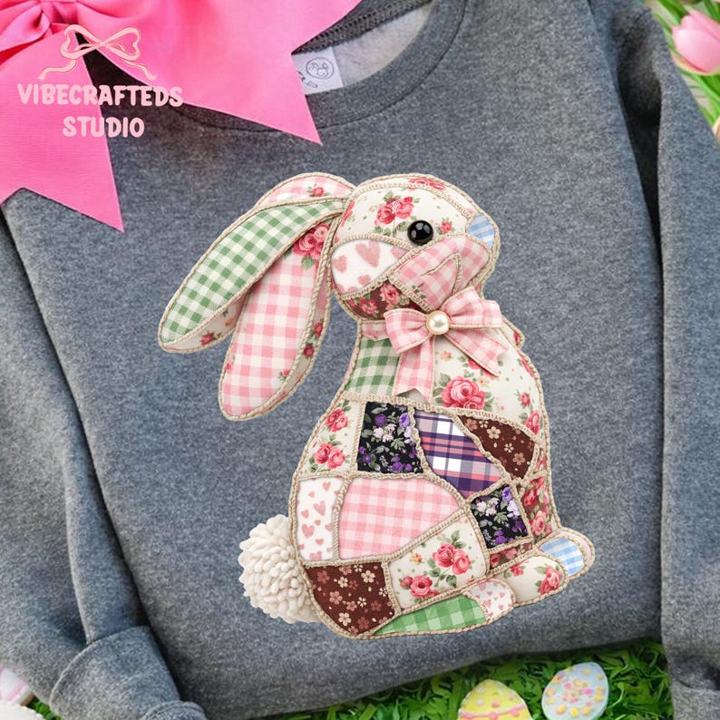 May include: A gray sweatshirt featuring a patchwork bunny design. The bunny is made of various patterned fabrics, including floral, gingham, and solid colors. A pink bow with a pearl accent adorns the bunny's neck. The text "VIBECRAFTEDS STUDIO" is visible.
