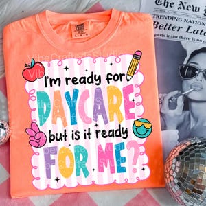 Pode incluir: Camiseta cor de pêssego com o texto "I'm ready for DAYCARE but is it ready FOR ME?" em letras coloridas e divertidas. O design inclui uma maçã, um lápis, um sinal de paz e um rosto sorridente com óculos de sol.